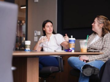 Two Madison Square Garden employees talking to each other in a conference room while sitting at a conference table.